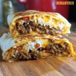 A Chicken Crunch Wrap cut in half, revealing seasoned ground chicken, rice, melted cheese, and diced tomatoes.