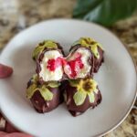 Close-up of chocolate-covered strawberry yogurt clusters, one cut open to reveal creamy filling and strawberries.