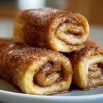 A stack of delicious Cinnamon Roll French Toast Roll-Ups, glistening with syrup and sprinkled with sugar.