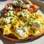 Close-up of Creamy Ricotta Egg Toast topped with fluffy scrambled eggs and fresh chives.