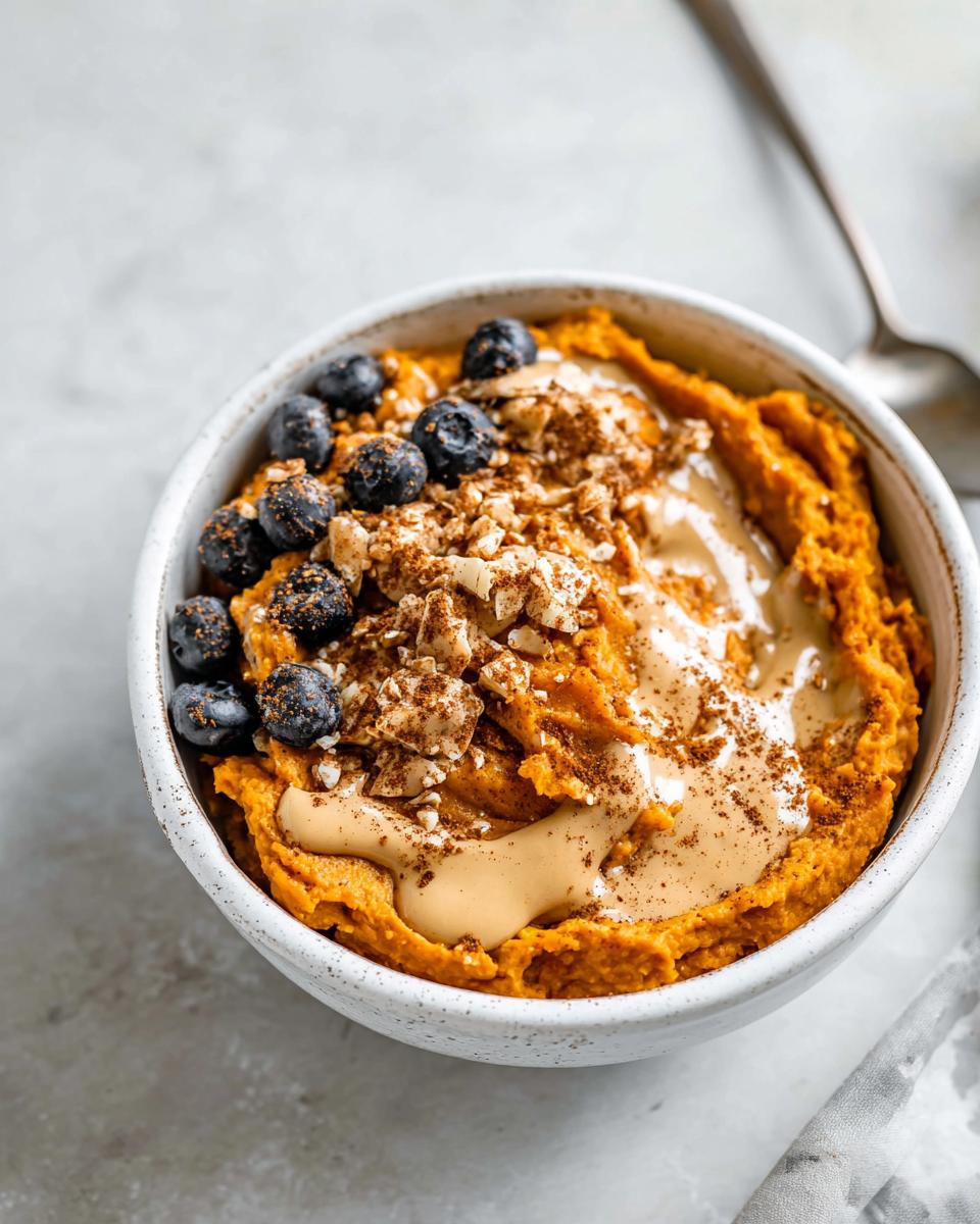 A Delicious Sweet Potato Breakfast Bowl topped with blueberries, nut butter, and chopped nuts.