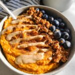 A close-up of a Delicious Sweet Potato Breakfast Bowl topped with blueberries, granola, and a drizzle of tahini.