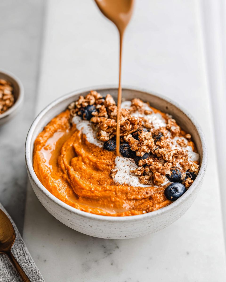 A Delicious Sweet Potato Breakfast Bowl being drizzled with sauce, topped with granola, blueberries, and yogurt.