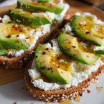 Close-up of EASY Avocado Toast with cottage cheese, sliced avocado, honey, and chili flakes on whole-grain bread.