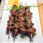 Close-up of three Easy Japanese Chicken Yakitori Skewers on a white plate, garnished with sesame seeds and chives.