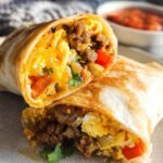 A close-up of two halves of an Effortless & Tasty Freezer Breakfast Burrito, filled with scrambled eggs, cheese, sausage, and peppers.