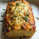 A close-up of a juicy garlic parmesan chicken meatloaf baked in a dish, topped with melted cheese and parsley.