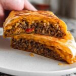 A close-up of a Grilled Cheese Burrito cut in half, revealing seasoned ground beef and rice filling with melted cheese.