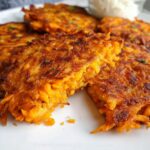 Close-up of golden-brown Healthy Sweet Potato Hash Browns on a white plate, with a small bowl of dip in the background.