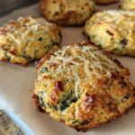 Close-up of golden brown High Protein Breakfast Biscuits topped with melted cheese and visible herbs.
