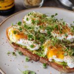 Two slices of toast topped with mashed avocado, poached eggs, sprouts, and chili flakes, a perfect high-protein breakfast.