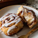 Close-up of a high-protein cinnamon roll bread, drizzled with white icing, with one piece broken open.