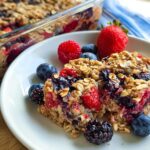 Two slices of High Protein Triple Berry Bake on a white plate, garnished with fresh berries.