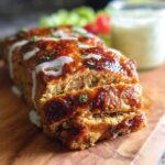 A close-up of a sliced Juicy Garlic Parmesan Chicken Meatloaf, drizzled with sauce and garnished with herbs.