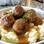 A bowl of Salisbury Steak Meatballs served over creamy Garlic Herb Mashed Potatoes, drizzled with gravy and garnished with parsley.