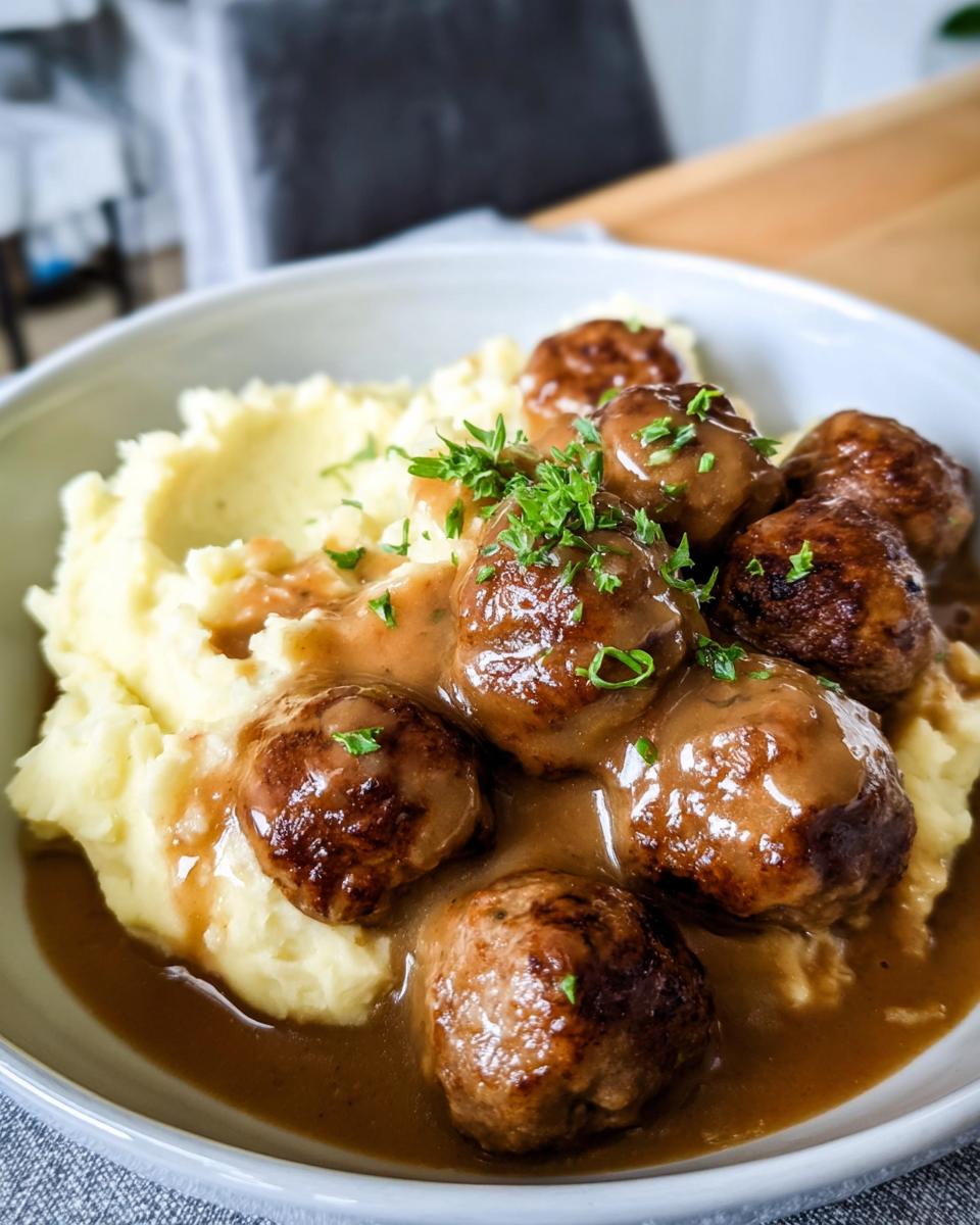 A close-up of Salisbury Steak Meatballs smothered in gravy, served with fluffy Garlic Herb Mashed Potatoes and garnished with parsley.