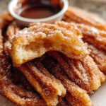 Close-up of Irresistible Spanish Churro Pancakes dusted with cinnamon sugar, with a small bowl of chocolate sauce in the background.