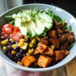 A vibrant Sweet Potato Taco Bowl filled with seasoned ground meat, roasted sweet potatoes, black beans, corn, tomatoes, avocado, and lettuce.
