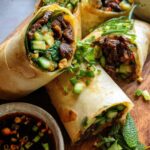 Close-up of golden-brown Thai Basil Beef Rolls filled with tender beef, cucumber, and herbs, served with a dipping sauce.