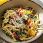 A close-up of a bowl filled with creamy Tomato Zucchini Pasta, topped with grated cheese and black pepper.