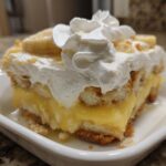 A slice of classic banana pudding with layers of vanilla wafers, creamy pudding, and homemade whipped cream, topped with banana slices.