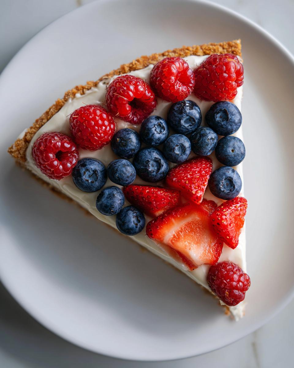 A slice of Fourth of July Flag Fruit Pizza on a cookie crust, topped with cream cheese frosting and fresh berries.