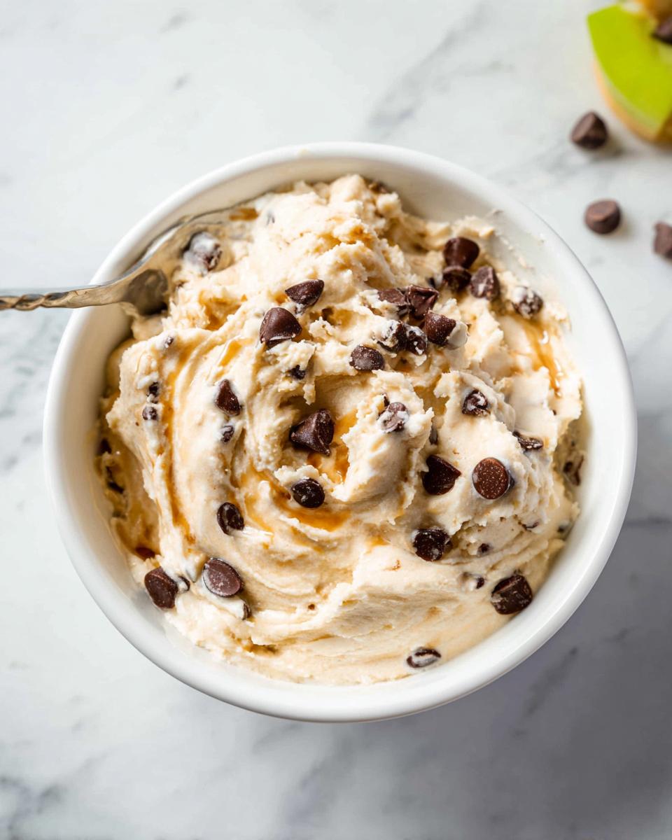 A bowl of creamy Greek Yogurt Cookie Dough recipe filled with chocolate chips and drizzled with caramel.