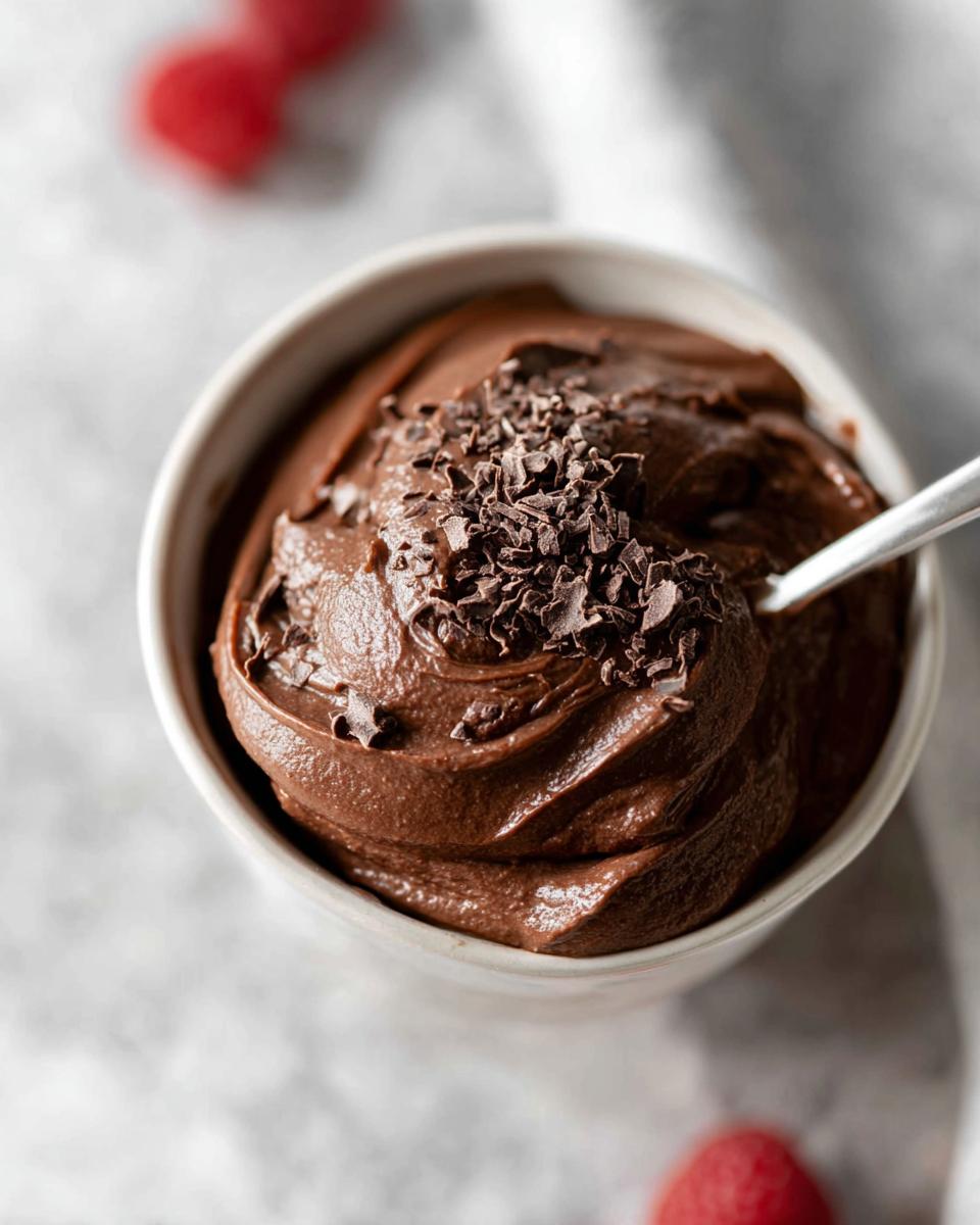 A close-up of a bowl filled with smooth, decadent High Protein Chocolate Pudding, topped with chocolate shavings and a spoon.
