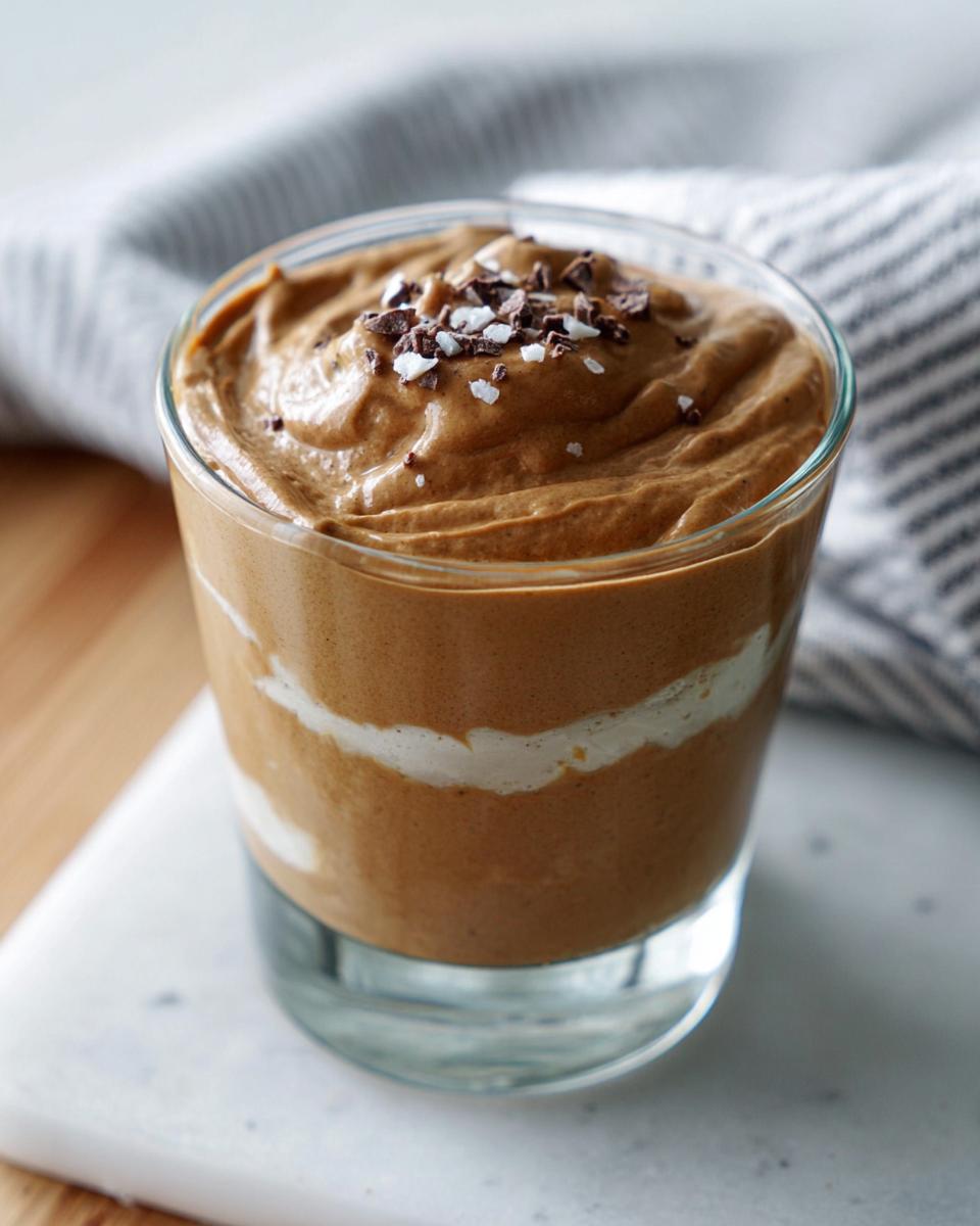 A close-up of a glass filled with High-Protein Cottage Cheese Peanut Butter Mousse, topped with chocolate shavings and sea salt.