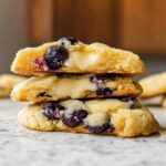 A stack of three delicious Lemon Blueberry Cheesecake Cookies, showing the creamy cheesecake filling and blueberries inside.