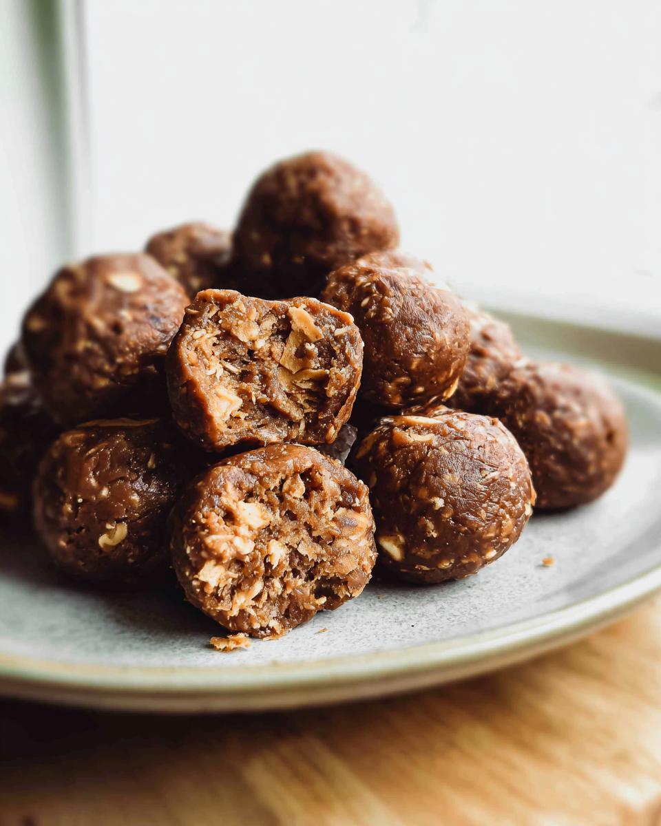 A pile of No-Bake Chocolate Peanut Butter Protein Balls on a plate, with one ball broken open to show the texture.