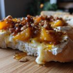 Close-up of a crostini topped with melted brie, baked peaches, and toasted pecans, a delicious peach recipe.