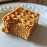 A single square of peanut butter fudge with a bite taken out, on a white plate. Perfect for dessert recipes.