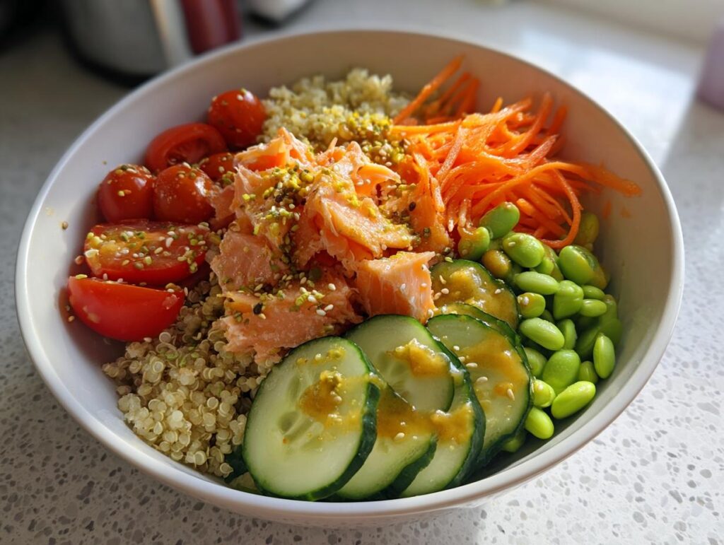 A vibrant salmon power bowl featuring quinoa, flaked salmon, cherry tomatoes, shredded carrots, edamame, and cucumber slices.