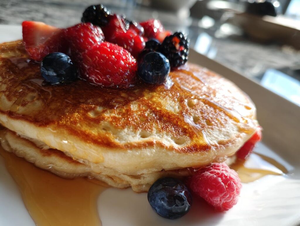 Stack of fluffy sheet pan pancakes topped with fresh berries and drizzled with syrup.