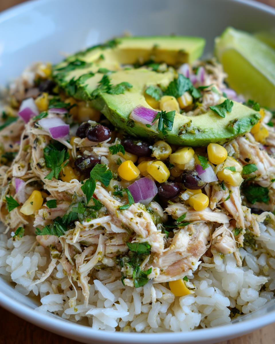 Close-up of a Slow Cooker Salsa Verde Chicken Taco Bowl with rice, shredded chicken, avocado, corn, black beans, and lime.
