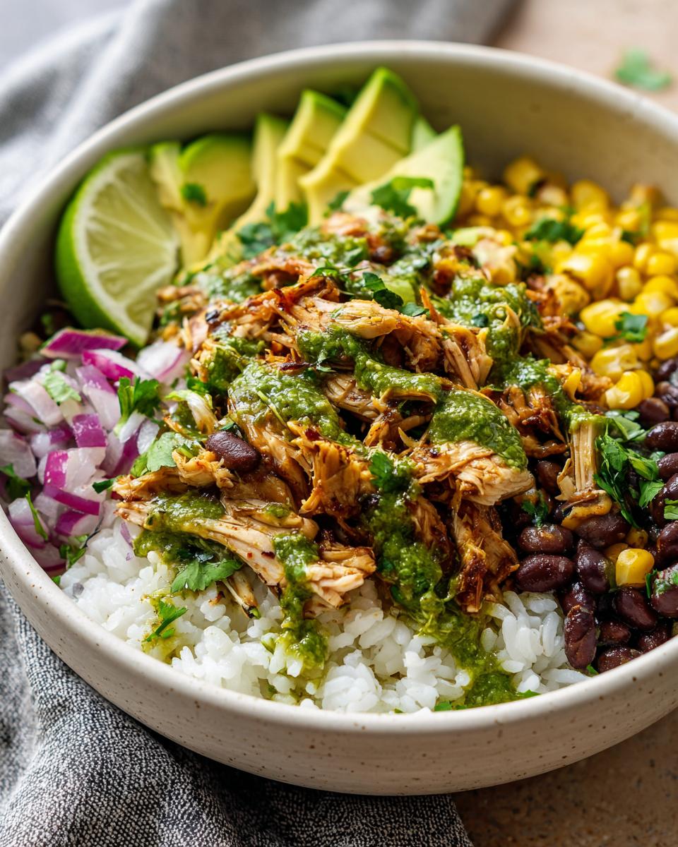 A close-up of a Slow Cooker Salsa Verde Chicken Taco Bowl filled with rice, shredded chicken, black beans, corn, avocado, lime, and red onion.