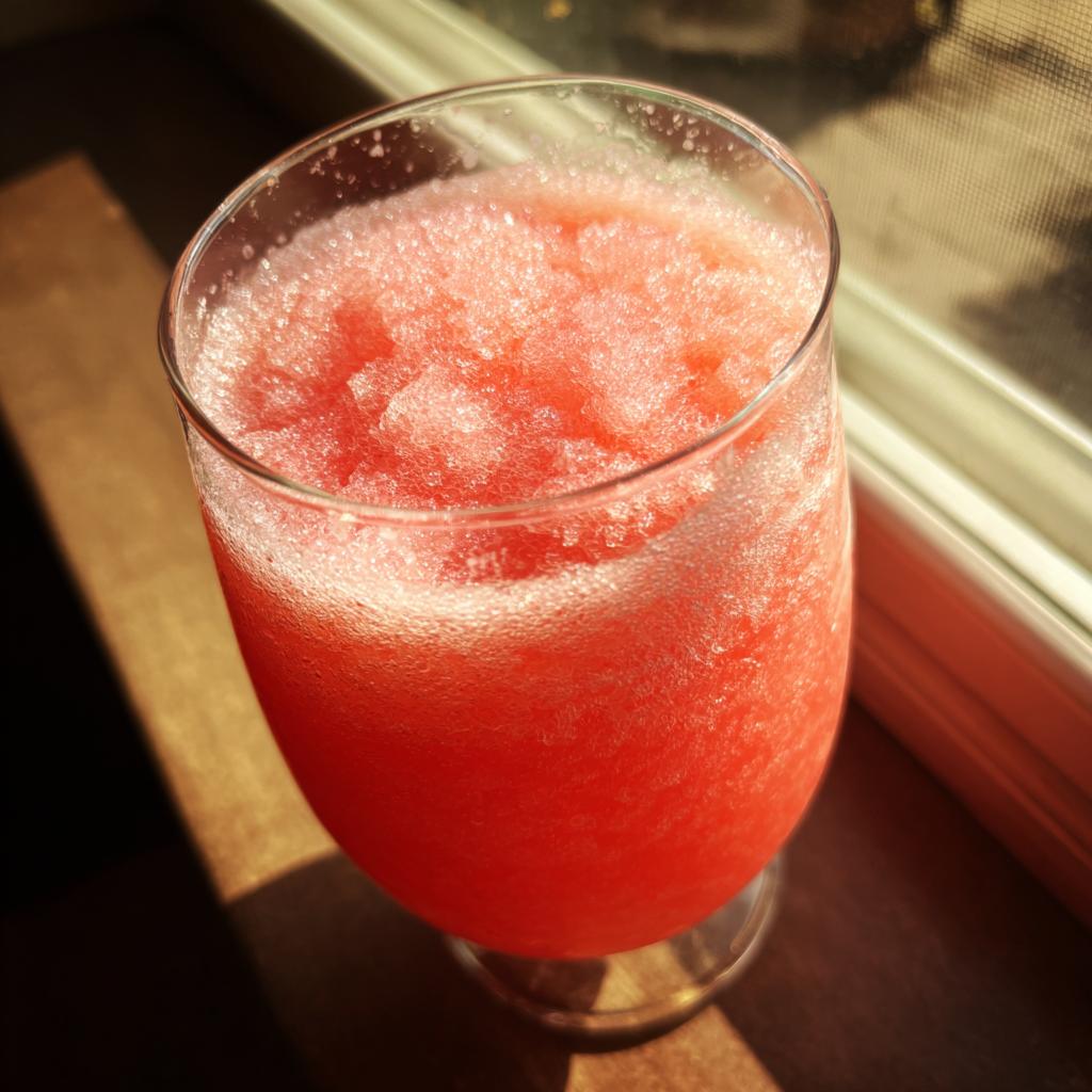 Close-up of a glass filled with a vibrant pink watermelon slushy, catching the sunlight.
